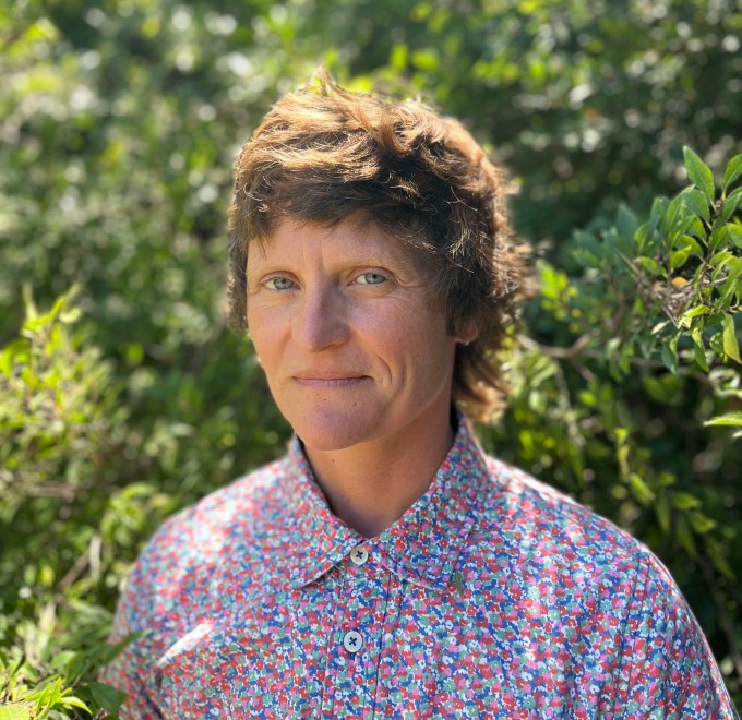 Headshot of Char Booth standing in front of greenery wearing a floral shirt. 